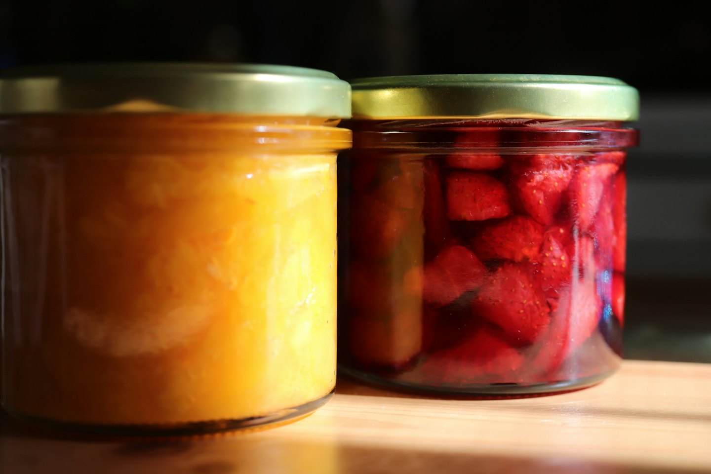 Ahşap bir masada duran iki kavanoz meyve reçeli.